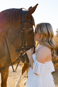 High school senior girl gently holding a horse in a sunlit field, lifestyle senior portrait session by Kaitlyn Dawn Photography.