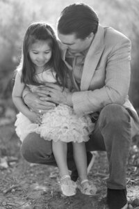 Black and white photo of a father from the Parker family holding his young daughter in a tender moment outdoors in Las Vegas, capturing a candid, emotional connection during a family portrait session.