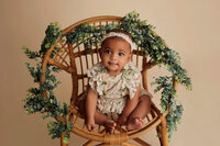 newborn baby in posed position in chair with green foliage prop during luxury studio session in Los Angeles