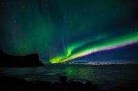 northern lights glow like neon green and purple streaks in the sky over the ocean at night