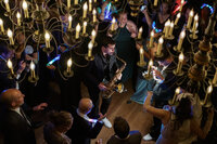 A high-energy, documentary style wedding photography shot of a saxophonist performing under a chandelier for a New York City celebration.