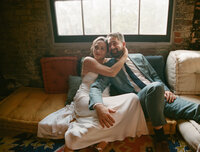 Bride and groom relaxing on couch indoors, embracing each other
