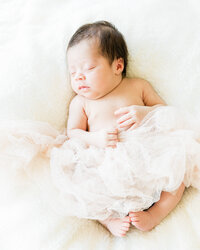 Sleeping newborn baby girl resting peacefully on a soft blanket with delicate tulle styling during an in-home newborn session.