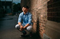 A boy from Oconomowoc High School squats next to a brick wall in Milwaukee's Third Ward at night.