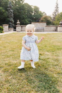 Toddler girl dressed in blue floral dress walking on grass during Toronto Family Photography session at Alexander Muir Memorial Gardens