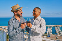 Two friends toasting drinks on a rooftop with a cityscape view, celebrating travel and good times.