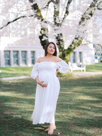 Latina woman in a white flowy getting cherry blossoms maternity photos done at UW Quad