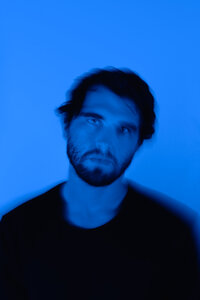 Independent music producer photographed in a blue-lit creative headshot for artist branding.