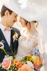 Bride and groom with their faces together underneath the bride's veil