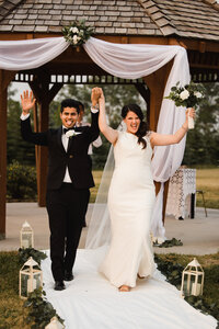 bride and groom cheer as they walk down the isle as newly weds, captured by Calgary wedding photographer Carly Hill
