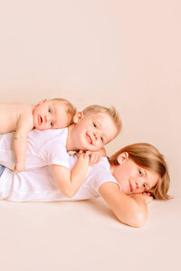Three children stacked together smiling during newborn family session in New Bern