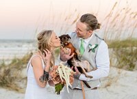 St. Augustine wedding capturing a beach of a bride and groom cradling their tiny brown puppy, a beloved part of their wedding day. - A portrait experience by Nature's Child Photography.