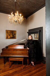Kent State graduate standing near a piano with a chandelier above her