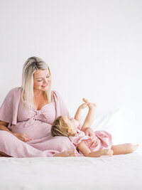 Pregnant mom looking over her toddler daughter who is being silly with her leg