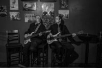 Two people with guitars sitting on stools playing together