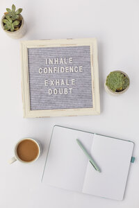 Inhale Confidence Exhale Doubt letter sign on desk with cup of coffee, succulent, notebook and pen.
