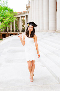 Senior girl wearing white dress standing on Wyatt Center stairs throwing Vanderbilt anchor down hand sign