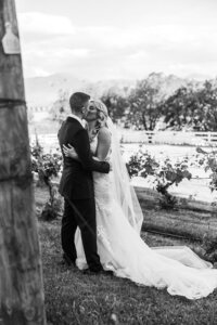 Black and white image of bride and groom kissing between rows of vines at Brindabella Hills Winery