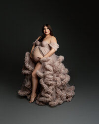 Pregnant woman posing in a dramatic blush ruffled maternity gown during an elegant studio maternity photography session highlighting her baby bump, photographed by Kaitlyn Dawn Photography.