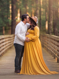 Expectant couple embracing on a wooded boardwalk during a maternity photography session in North Carolina