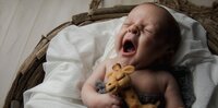 In St. Johns, a newborn lets out a wide, sleepy yawn while clutching a tiny stuffed giraffe, photographed during a cozy in-home lifestyle newborn. - A portrait experience by Nature's Child Photography.