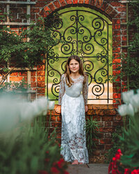 Child in white lace dress standing in front of ornate iron gate at Tryon Palace in New Bern North Carolina