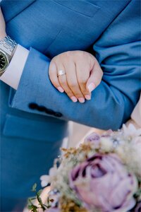 closeup of the engagement ring featuring the grooms pastel blue jacket purple flowers and white shirt