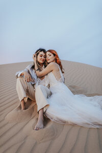 Wedding portrait of two people seated together on sand dunes during an outdoor destination wedding session.