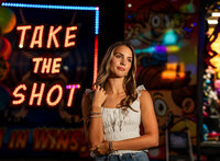 Senior portrait at the Greater Gulf State Fair in Mobile, Alabama — looking to the side with a
“Take Your Shot” sign glowing behind her.