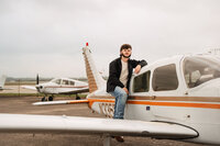 Senior portrait at a small hangar near Mobile International Airport in Mobile, Alabama —
standing on the airplane stairs with his arm resting on the plane.