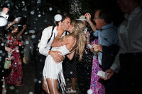 couple shares a kiss as they exit their wedding with confetti flying around them