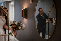 Marié ajustant son veston devant un miroir rond doré, bouquet de la mariée en premier plan, préparatifs au Fairmont, Montréal