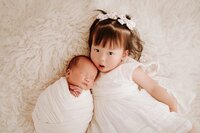 Newborn baby sleeping while being gently held by older sibling under 3