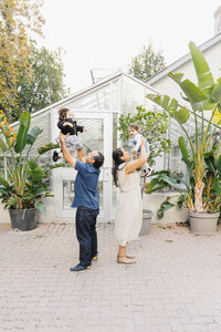 Parents tossing young daughters in the air during family session in a Toronto botanical garden.