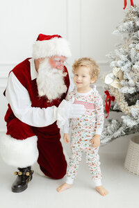 Santa holding a baby boy as they pose in front of a christmas tree