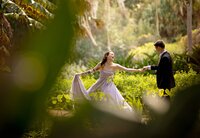 Professional photography by Nature's Child Photography: In Palm Coast, an engaged couple playfully reaches for each other in a sunlit garden, her dress sweeping outward as she laughs mid-step.