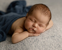 Sleeping newborn baby boy posed with hands under chin on a soft gray blanket during a studio newborn photography session by Yucaipa newborn photographer Kaitlyn Dawn Photography.