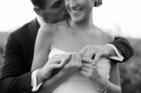 the groom tenderly kissing the bride’s shoulder while holding her hands