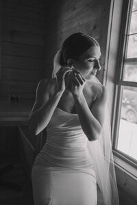 bride sitting in front of a windor putting on her earrings