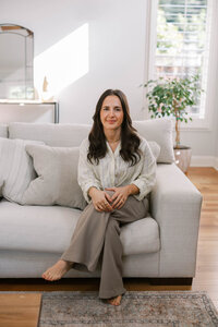 Woman sitting on a couch and with her hands softly in her lap, while posing for her bay area branding photography photoshoot
