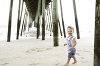 Charleston Baby Milestone Photographer - Baby laughs as he runs along the beach during his Milestone Portrait Session at Holy City Babies Portrait Studio in Charleston, SC.