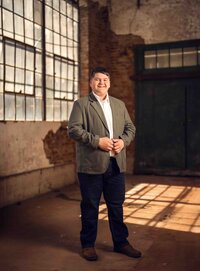Senior boy in a gray dress shirt and black pants posing inside an industrial building at Sloss Furnaces in Birmingham, Alabama.