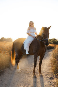 High school senior girl riding a horse along a dirt path during sunset, lifestyle senior portrait session by Kaitlyn Dawn Photography.