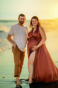 Expectant parents standing together on the beach during sunset maternity portraits in Atlantic Beach North Carolina