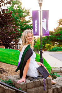 College graduate sitting on wall with Trevecca banner behind her