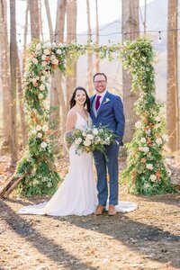 Bride and groom under winter ceremony arbor with ivory and orange florals by Flowergirl Cville at Indigo House, Afton, VA | Photo by Xiaoqi Li Photography