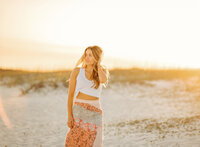 Senior portrait on the beach in Gulf Shores, Alabama — sunset glow behind her with a sun flare.