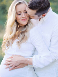 Close-up of a husband kissing his pregnant wife while holding hands