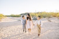Three children from the Collins family walking hand in hand through the Las Vegas desert at golden hour, sharing a joyful and playful sibling moment during an outdoor family photo session.