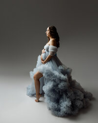 Pregnant mom in a flowing blue tulle gown posing in profile, highlighting her baby bump during a maternity photoshoot by Kaitlyn Dawn Photography in Yucaipa.